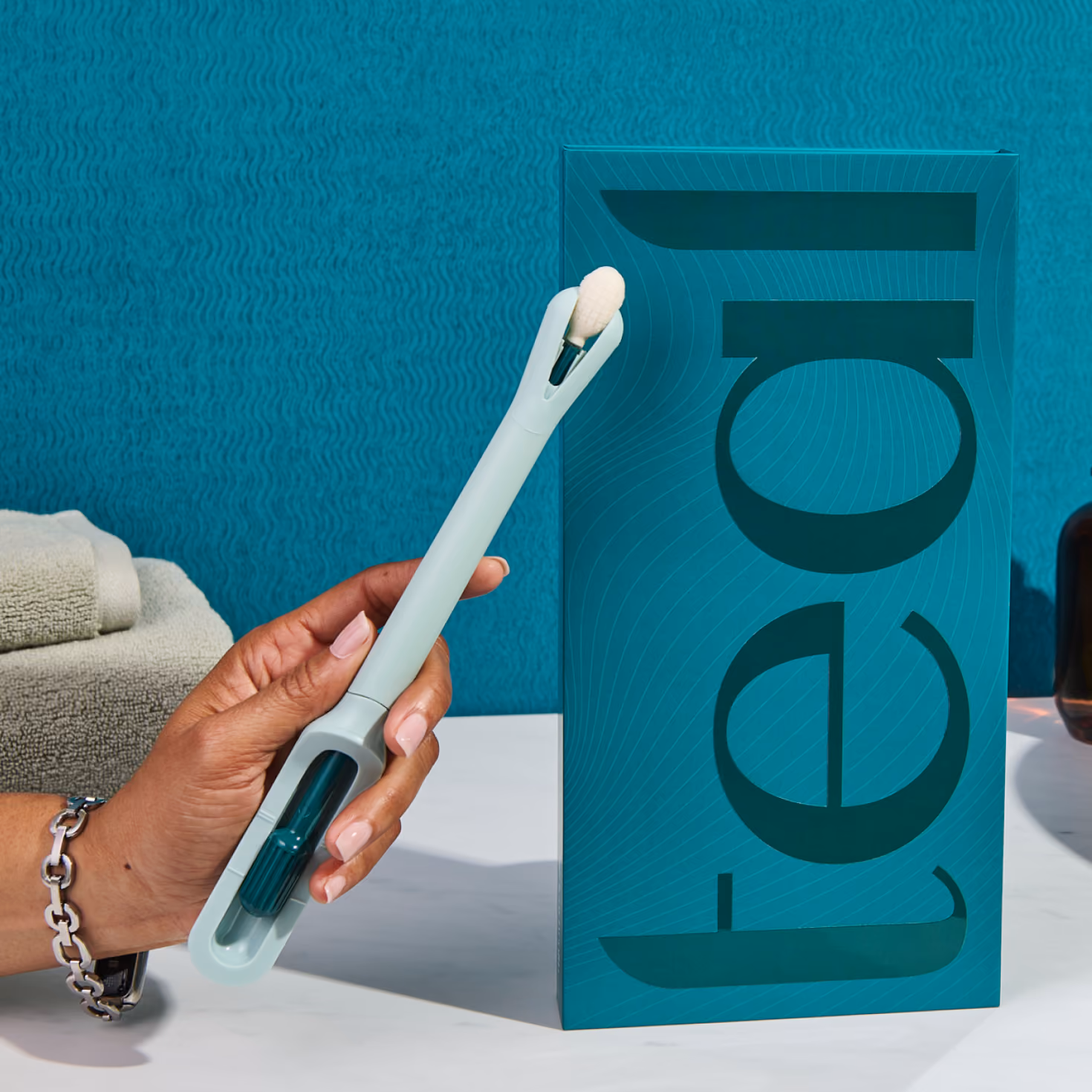 A hand holding the Teal Wand next to its packaging